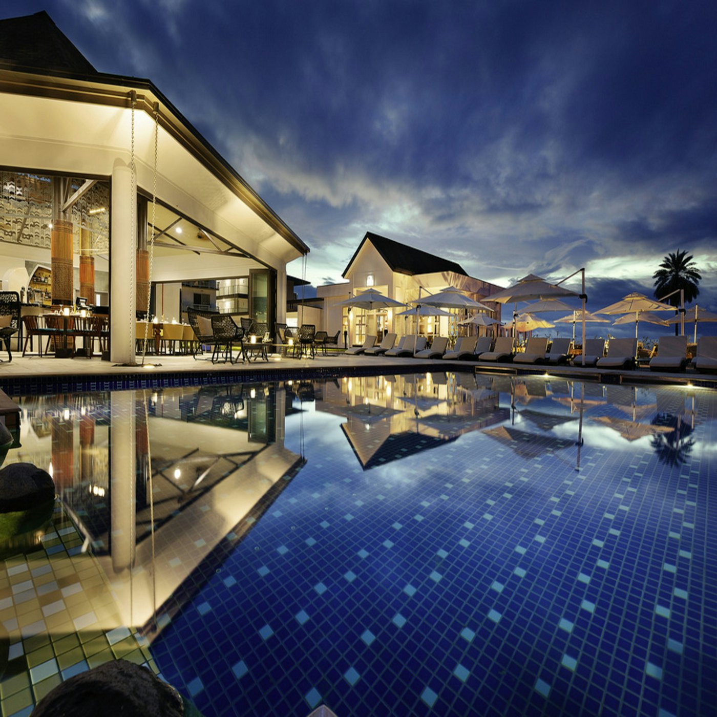 A resort swimming pool at dusk on Phuket, with lounge chairs and a lit poolside bar — the kind of venue whose finances these consultations address.